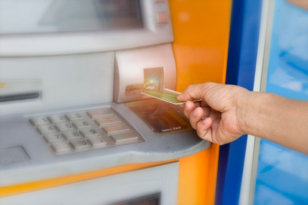 A person is inserting hand ATM card into bank machine to withdraw money